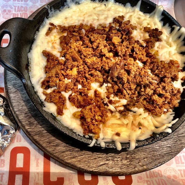 Melted white cheese and ground chorizo in a black cast iron skillet on a wooden board.