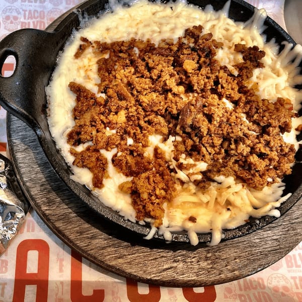 Melted white cheese and browned chorizo in a black cast iron skillet on a wooden board.