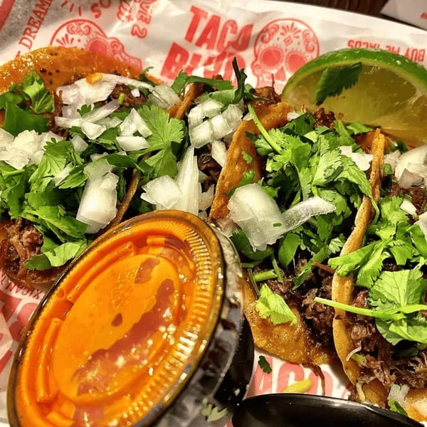 Three Taco Blvd tacos with meat, cilantro, onions, a lime wedge, and a side of sauce.