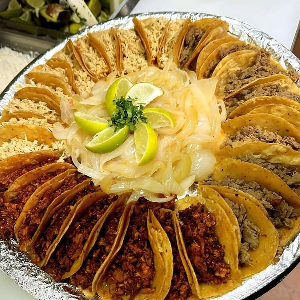 A large platter of various tacos, including chicken, beef, and pork, with a center of onions and lime.