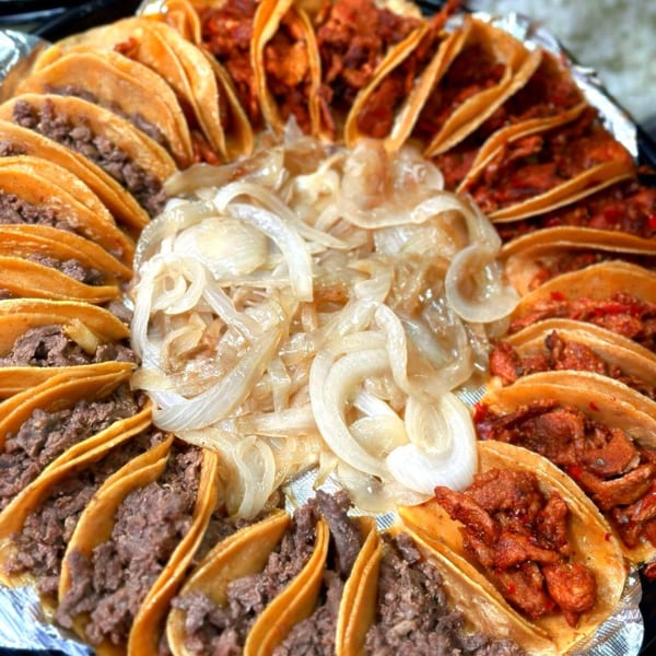 A platter of Taco Blvd tacos with various fillings and a pile of caramelized onions in the center.