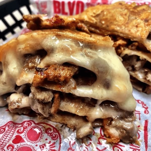 Close-up of a cheesy Taco Blvd quesadilla with meat filling, served in a basket.